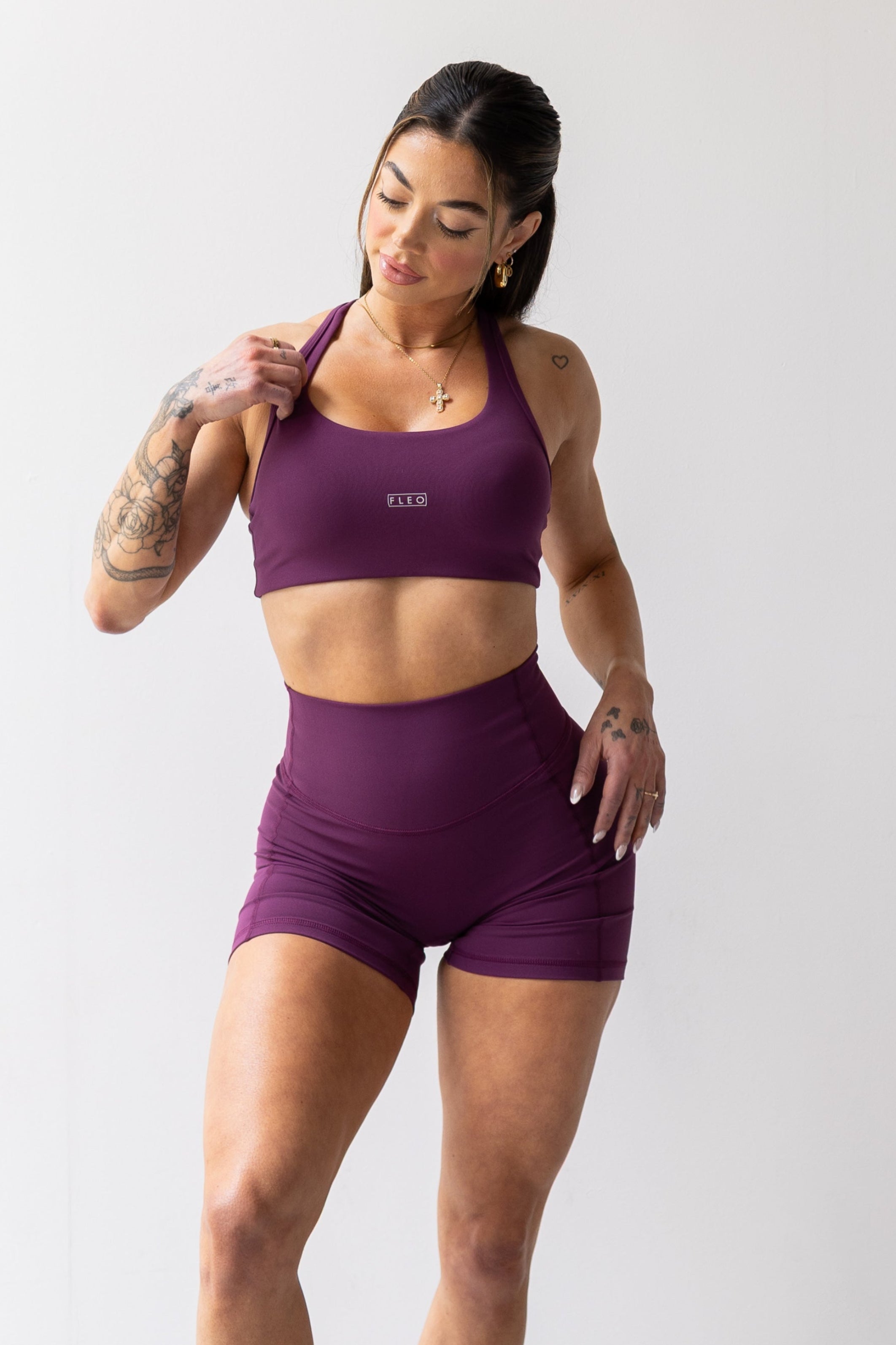 Woman wearing a purple sports bra and shorts set with white sneakers on a white background